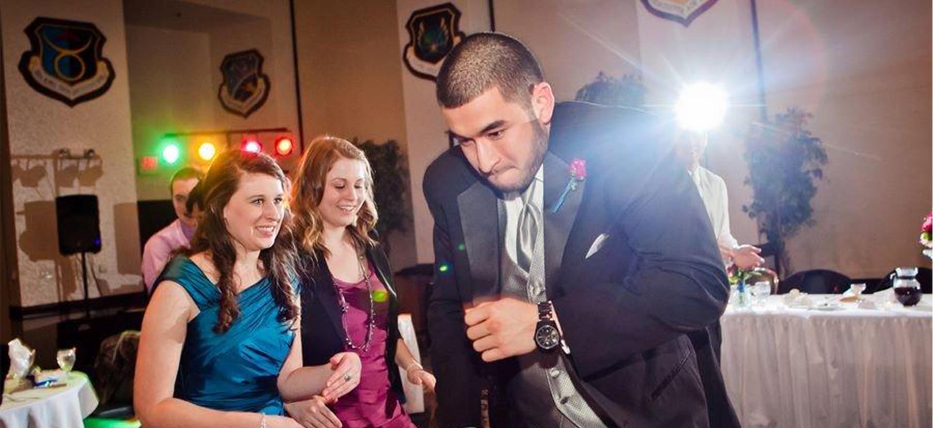 Young man in tux doing a silly 'jogging' dance with girl in blue dress and girl in magenta dressing looking on cautiously.